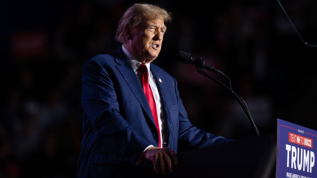 Trump speaks at a podium with his campaign logo and slogan.